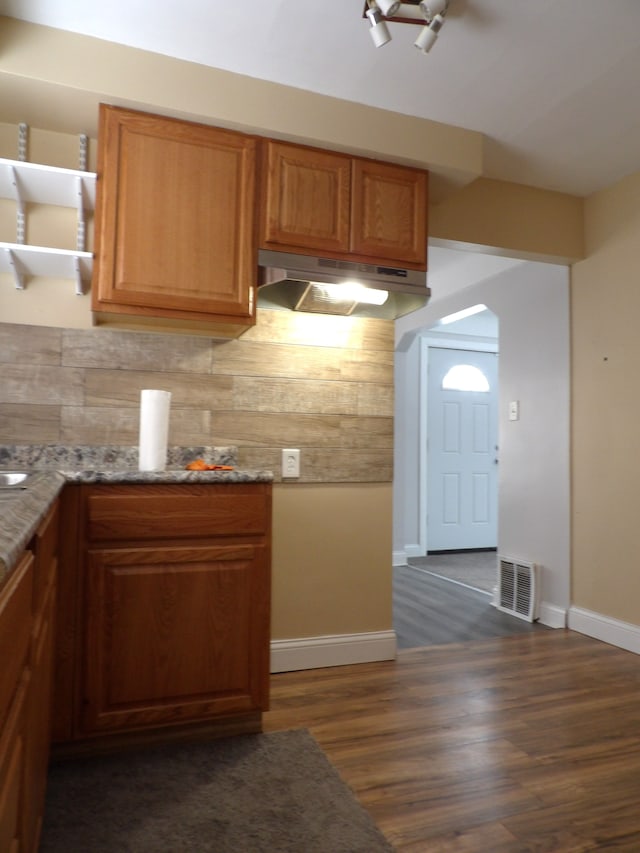 kitchen with brown cabinetry, backsplash, visible vents, and under cabinet range hood