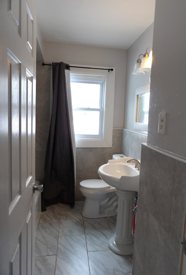 bathroom featuring marble finish floor, toilet, and tile walls