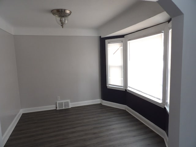 empty room with visible vents, dark wood finished floors, and baseboards