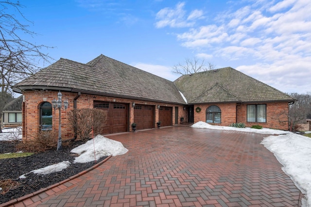 french country inspired facade with brick siding, decorative driveway, and a garage