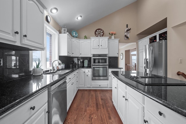 kitchen with a sink, stainless steel appliances, white cabinetry, and vaulted ceiling