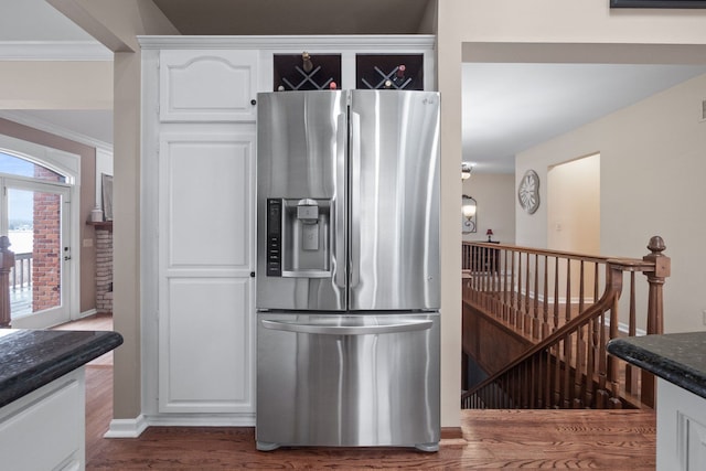 kitchen featuring ornamental molding, wood finished floors, white cabinetry, dark stone counters, and stainless steel fridge with ice dispenser