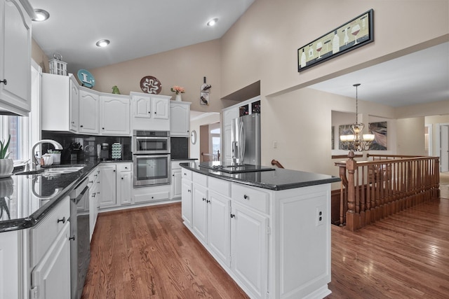 kitchen with a sink, appliances with stainless steel finishes, white cabinets, an inviting chandelier, and dark wood-style flooring