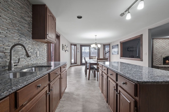 kitchen featuring a sink, a kitchen island, a fireplace, decorative backsplash, and hanging light fixtures