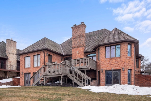 rear view of property featuring brick siding, a wooden deck, stairs, a lawn, and a chimney