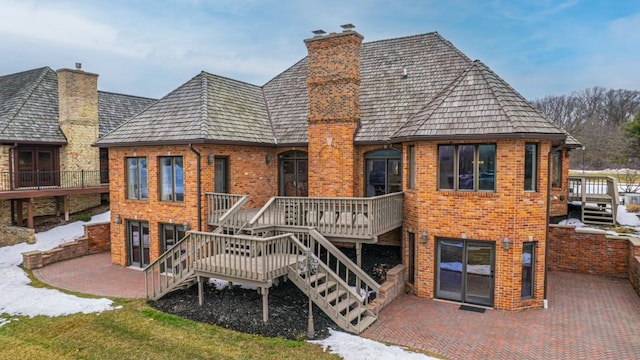 rear view of property featuring a patio, brick siding, a deck, and a chimney