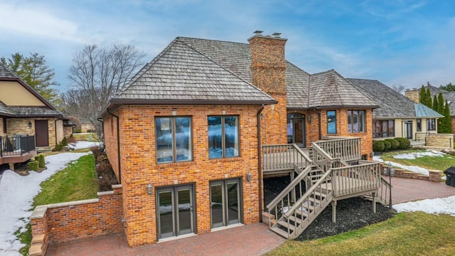 back of house with a deck, a patio, brick siding, and a chimney