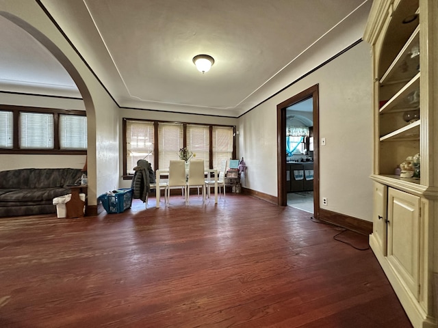 unfurnished room featuring arched walkways, ornamental molding, dark wood finished floors, and baseboards