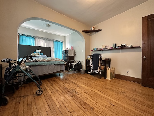 bedroom featuring light wood-style flooring, arched walkways, and baseboards