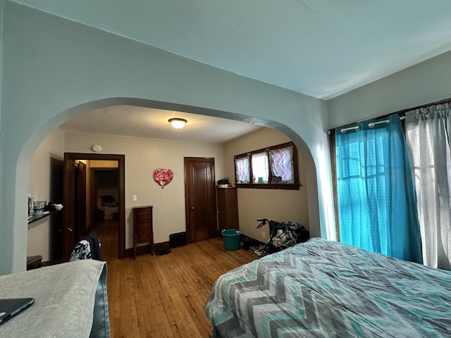 bedroom with arched walkways, wood-type flooring, and baseboards