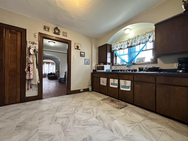 kitchen featuring arched walkways, stainless steel microwave, dark countertops, and a wealth of natural light