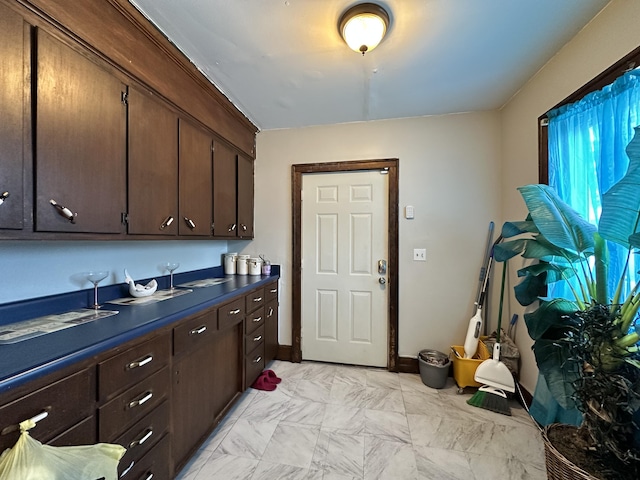 kitchen with marble finish floor, dark brown cabinets, dark countertops, and baseboards