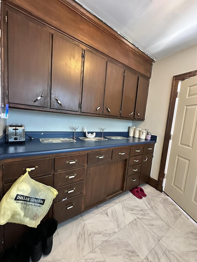 kitchen with marble finish floor, dark countertops, dark brown cabinetry, and a toaster