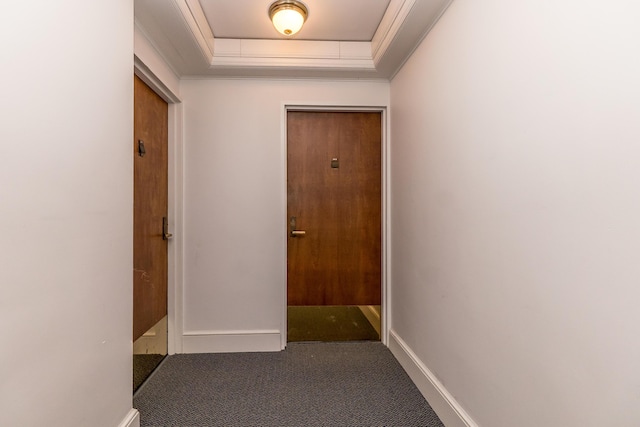 corridor with baseboards, a raised ceiling, crown molding, and dark colored carpet