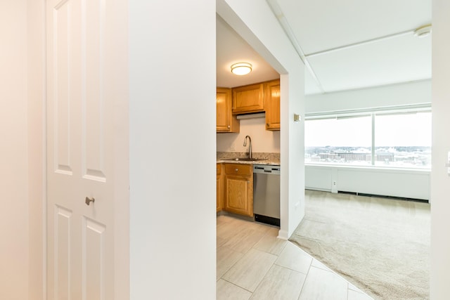 kitchen featuring light countertops, stainless steel dishwasher, brown cabinetry, light carpet, and a sink