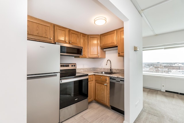 kitchen with brown cabinetry, appliances with stainless steel finishes, light countertops, and a sink