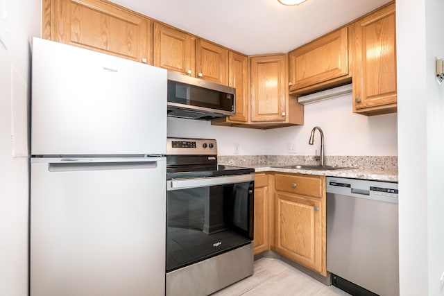 kitchen with appliances with stainless steel finishes, brown cabinetry, and a sink