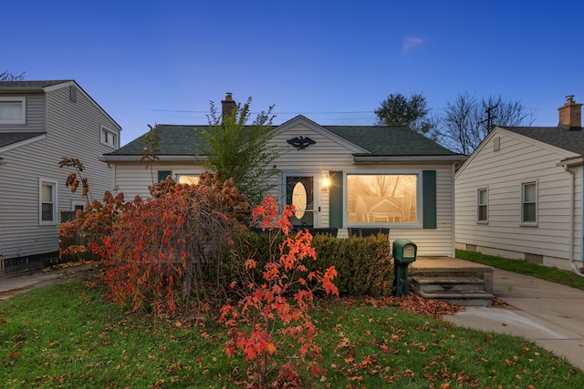 view of front of house with a shingled roof, a yard, and a chimney