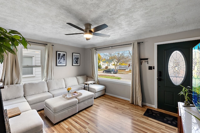 living room featuring a textured ceiling, light wood finished floors, a ceiling fan, and baseboards