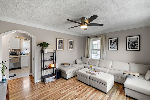 living area featuring light wood-style floors, ceiling fan, and a textured ceiling