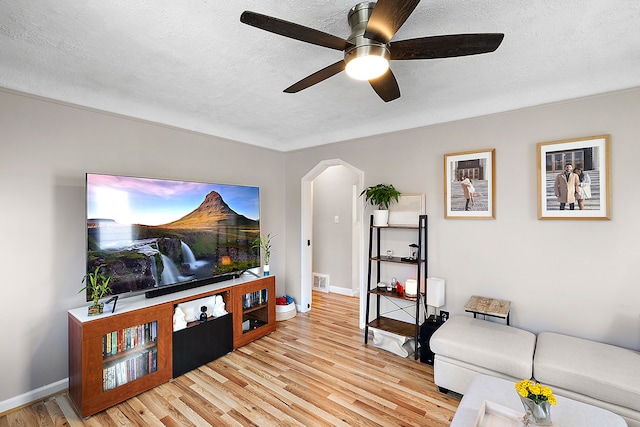 living area featuring arched walkways, baseboards, a textured ceiling, and light wood finished floors