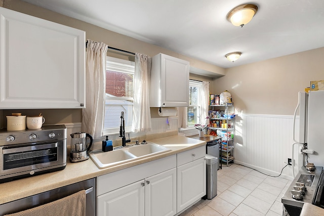 kitchen with light countertops, freestanding refrigerator, wainscoting, a sink, and white cabinetry