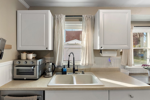 kitchen featuring a wainscoted wall, white cabinetry, light countertops, and a sink