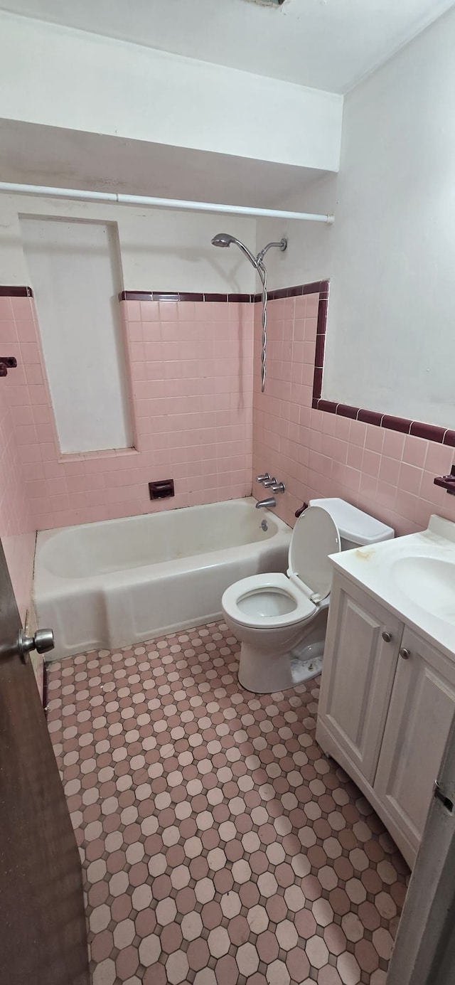 bathroom featuring toilet, a wainscoted wall, vanity, tile walls, and shower / bathing tub combination