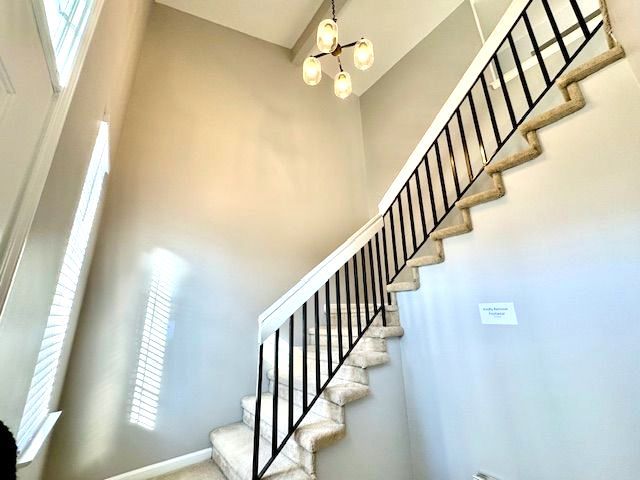 stairway featuring a towering ceiling, an inviting chandelier, and baseboards