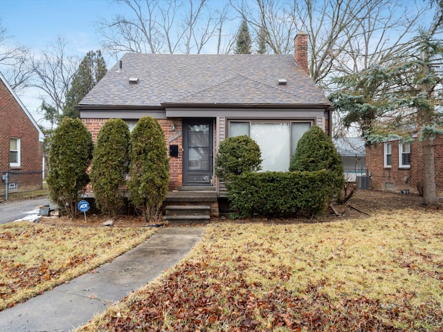 bungalow with a chimney, roof with shingles, central air condition unit, a front lawn, and brick siding