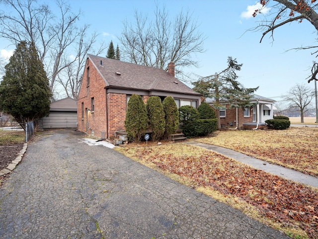 view of front facade featuring brick siding, an outdoor structure, fence, a detached garage, and a chimney