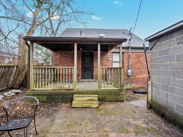 rear view of house with covered porch, brick siding, and roof with shingles