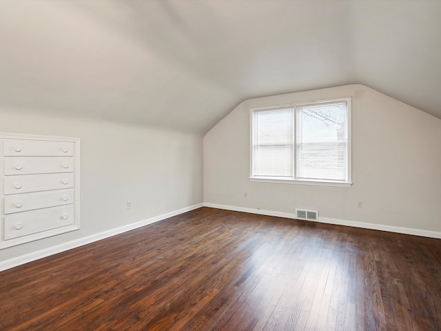 additional living space featuring vaulted ceiling, dark wood-style flooring, visible vents, and baseboards