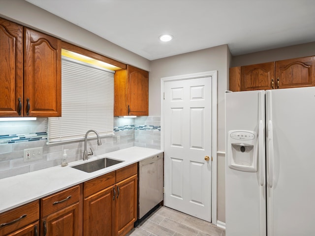 kitchen featuring decorative backsplash, a sink, light countertops, white fridge with ice dispenser, and stainless steel dishwasher