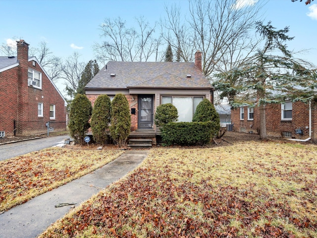 view of front of house with roof with shingles, a chimney, a front lawn, and brick siding