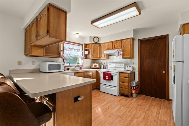 kitchen featuring under cabinet range hood, a peninsula, white appliances, light countertops, and brown cabinets