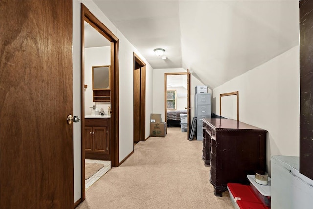 corridor featuring light carpet, baseboards, a sink, and lofted ceiling