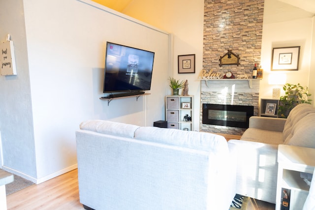 living room featuring a stone fireplace, baseboards, and wood finished floors