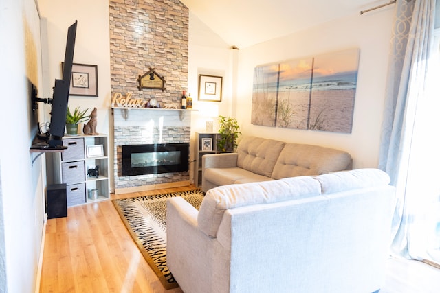 living room with vaulted ceiling, wood finished floors, and a stone fireplace