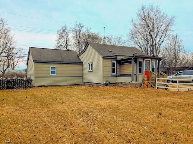 back of house with a shingled roof, a lawn, and fence