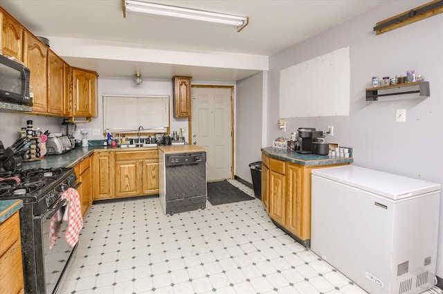 kitchen featuring dark countertops, brown cabinets, light floors, black appliances, and a sink