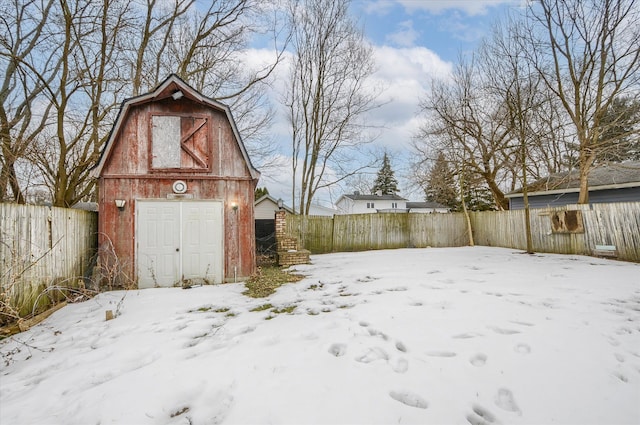 yard layered in snow featuring a barn, a fenced backyard, a detached garage, and an outbuilding