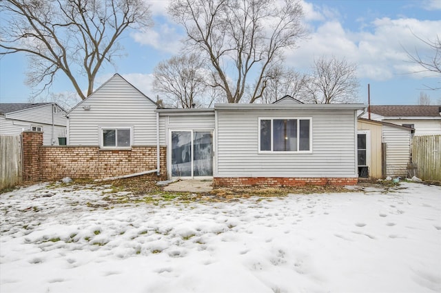 snow covered rear of property with fence and brick siding