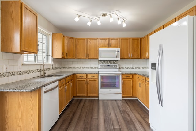 kitchen with white appliances, dark wood-type flooring, a sink, decorative backsplash, and dark stone counters