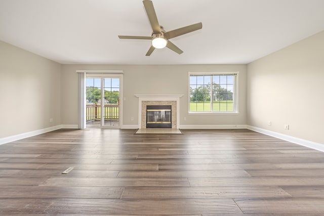 unfurnished living room featuring ceiling fan, a premium fireplace, wood finished floors, and baseboards