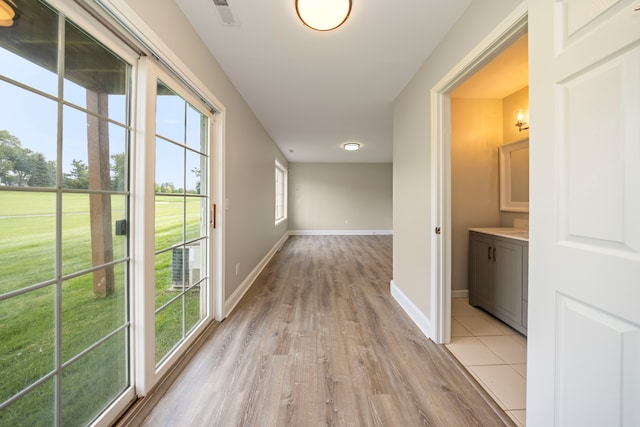 hall with baseboards, visible vents, and light wood finished floors