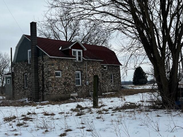 view of snowy exterior with a garage, stone siding, and a gambrel roof