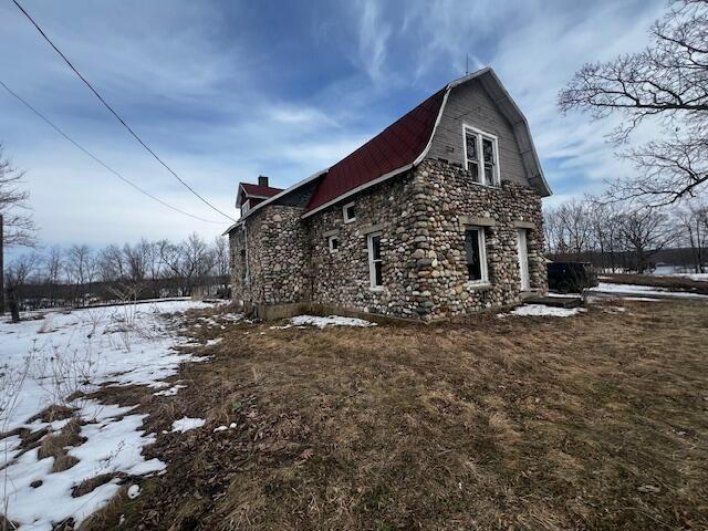 view of snowy exterior with a barn, stone siding, and a gambrel roof