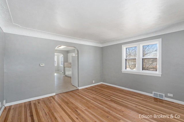 spare room with light wood-type flooring, arched walkways, visible vents, and baseboards