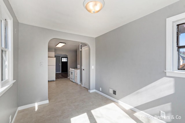 spare room featuring baseboards, visible vents, and arched walkways